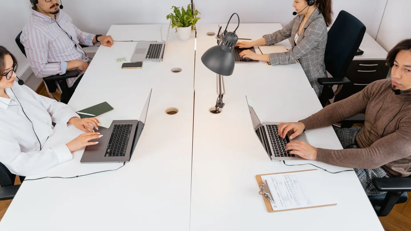 Support team wearing headsets while clearing customer ticket backlog from shared workstations.